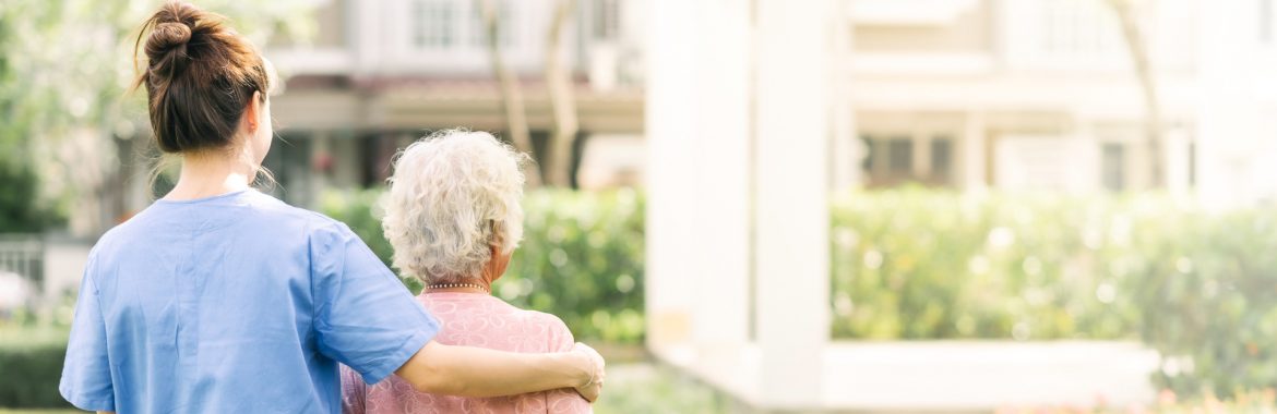 Kimihia Home & Hospital, Back view of nurse caregiver support walking with elderly woman outdoor