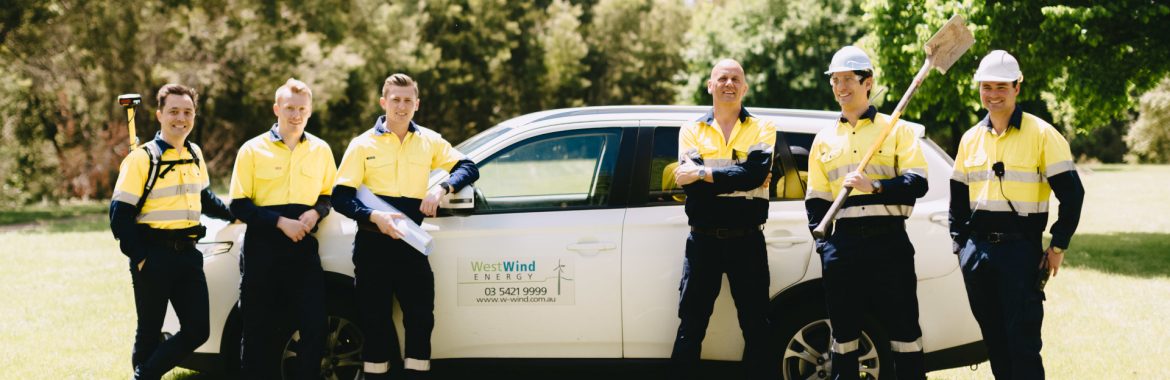 WestWind Energy employees posing for a group photo by a car with the WestWind logo.